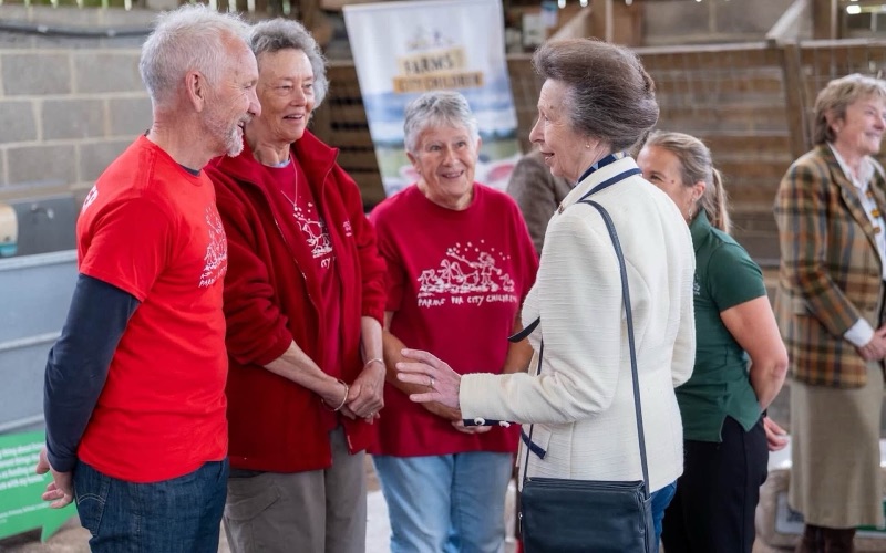 Princess Anne in conversation with three people in red tops bearing the charity