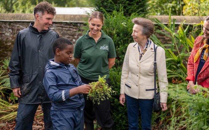 A boy shows a handful of green plants to Princess Anne in an old walled garden