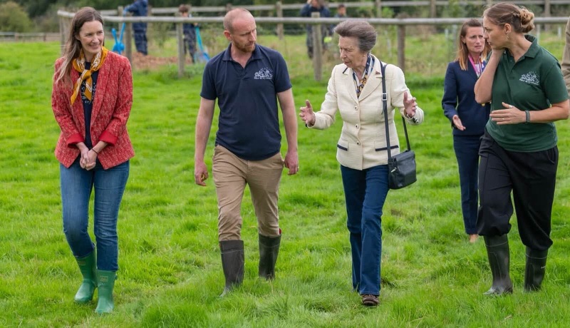 Princess Anne walks across a field with farm staff in wellington boots