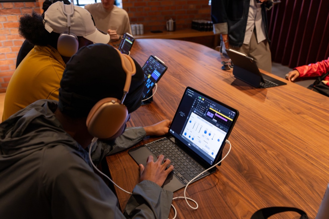 Unge deltakere med hodetelefoner arbeider med musikkprogramvare på nettbrett rundt et bord