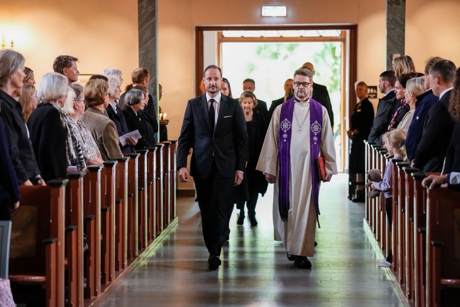Kong Haakon går ned midtgangen i Asker kirke sammen med presten, med dronning Sonja bak seg