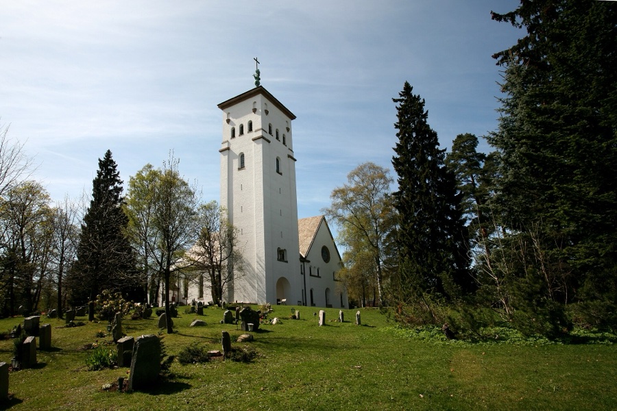 Ris Church, a white long church with a tall square tower, seen from the churchyard with gravestones and spruce trees around it