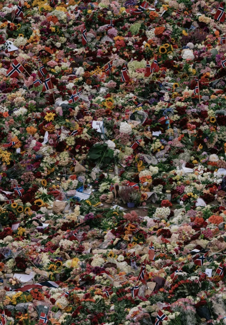 Nærbilde av blomsterhavet på Slottsplassen med norske flagg, lys, bamser og hilsener mellom blomstene