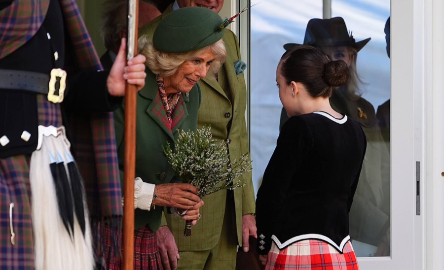 Queen Camilla receives a bouquet of white heather from a girl in a black velvet jacket and red tartan skirt