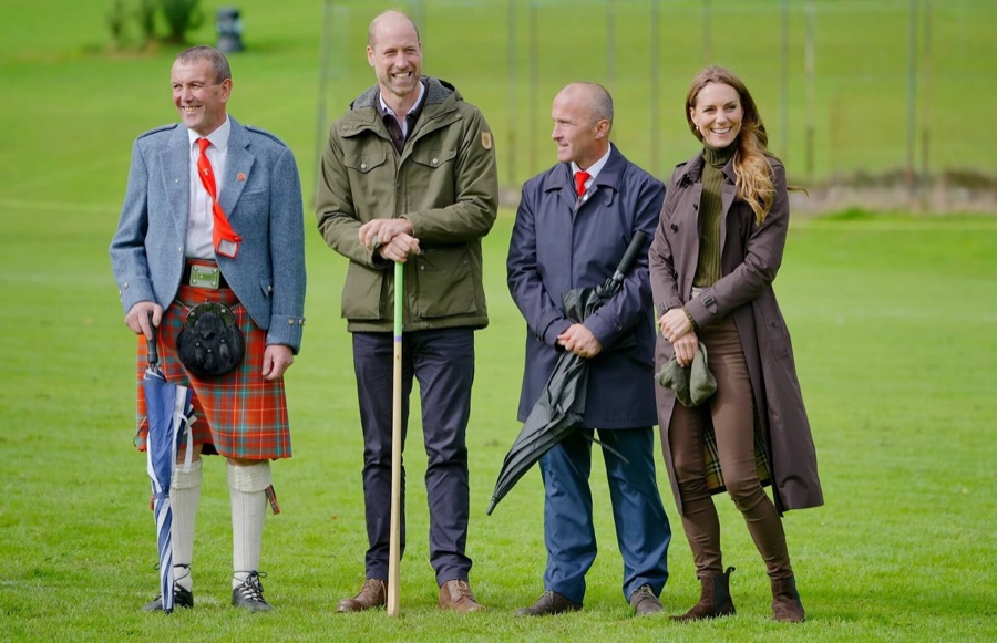 Prince William holding a shinty stick stands with Princess Catherine and two men on a grass pitch