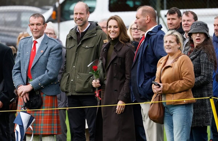 Prince William and Princess Catherine stand in a crowd along the pitch, the Princess holding a red rose