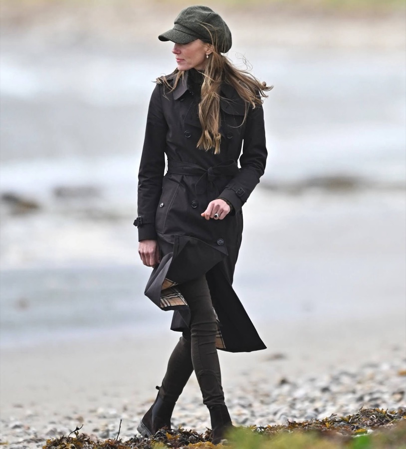 Princess Catherine in a brown trench coat and green cap walks along a stony beach