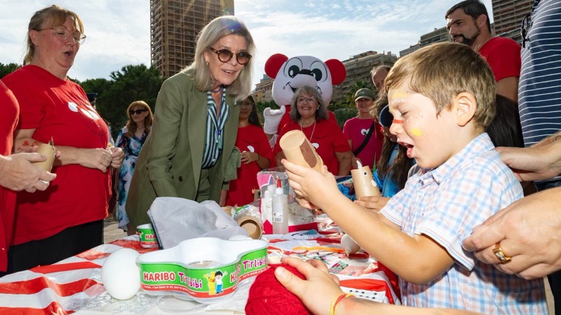 Princess Caroline stands at a table where a boy with face paint glues together a figure