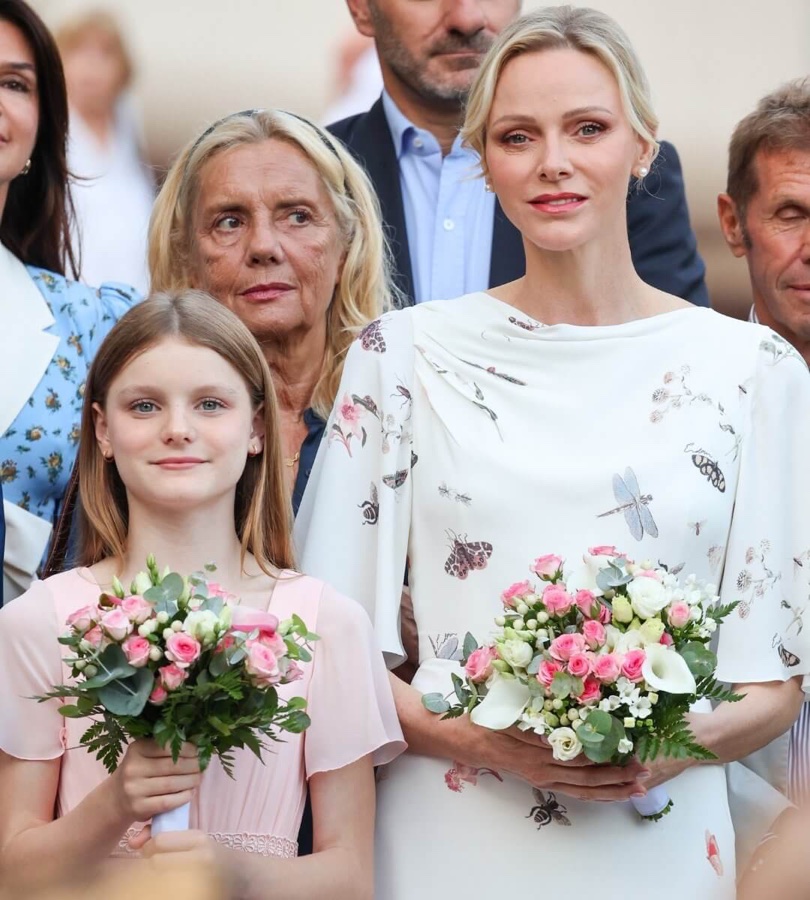 Fyrstinne Charlène i hvit kjole med insektmønster og prinsesse Gabriella i lyserosa kjole, begge med blomsterbuketter