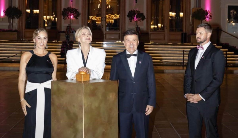 Princess Charlène places her hands on a golden button on a plinth in front of the casino, flanked by three people