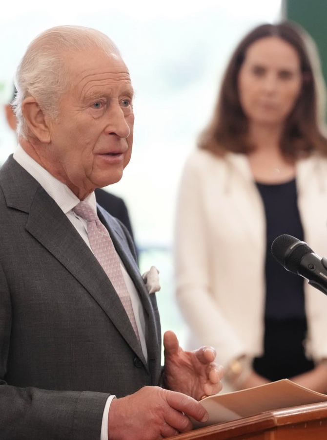 King Charles in a grey suit speaks from behind a lectern with a microphone