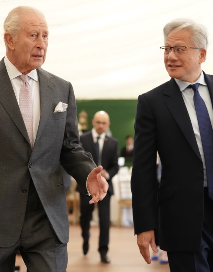 King Charles in a grey suit walks beside a man in a dark suit and glasses inside the marquee