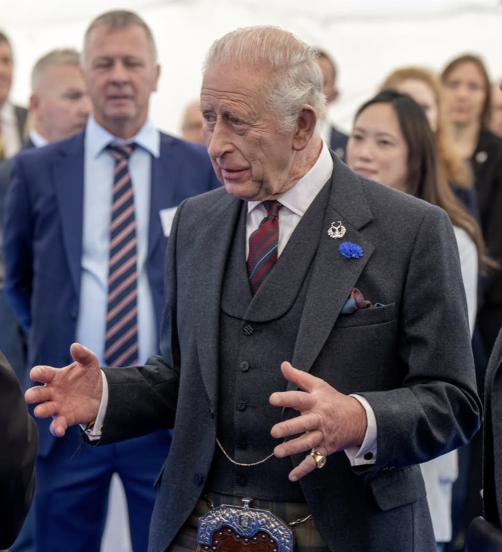 Kong Charles gestikulerer mens han snakker med flere personer under et telttak