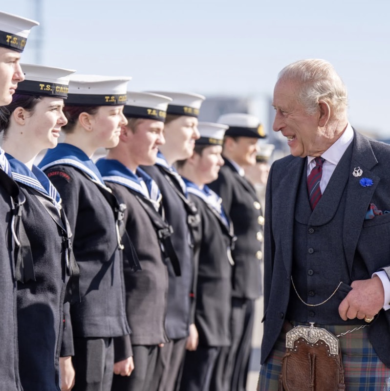 Kong Charles går langs en rekke sjøkadetter i uniform og hvite luer og snakker med dem