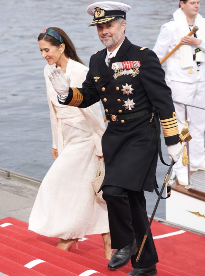 King Frederik waves as he walks down the gangway on the red carpet, with Queen Mary behind him