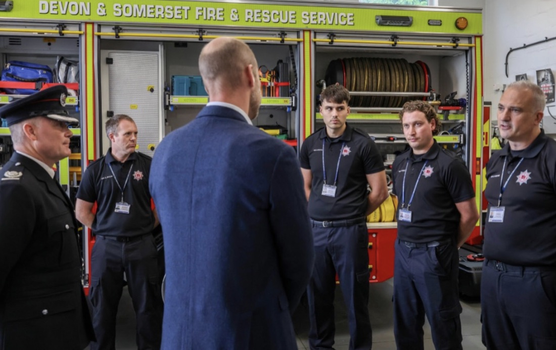 Prins William står med ryggen til og snakker med en gruppe brannmannskaper foran en brannbil fra Devon and Somerset Fire and Rescue Service
