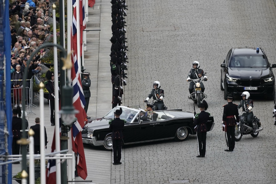 Kong Haakon ankommer Stortinget i den åpne Lincoln Continental, med gardister og politi rundt bilen