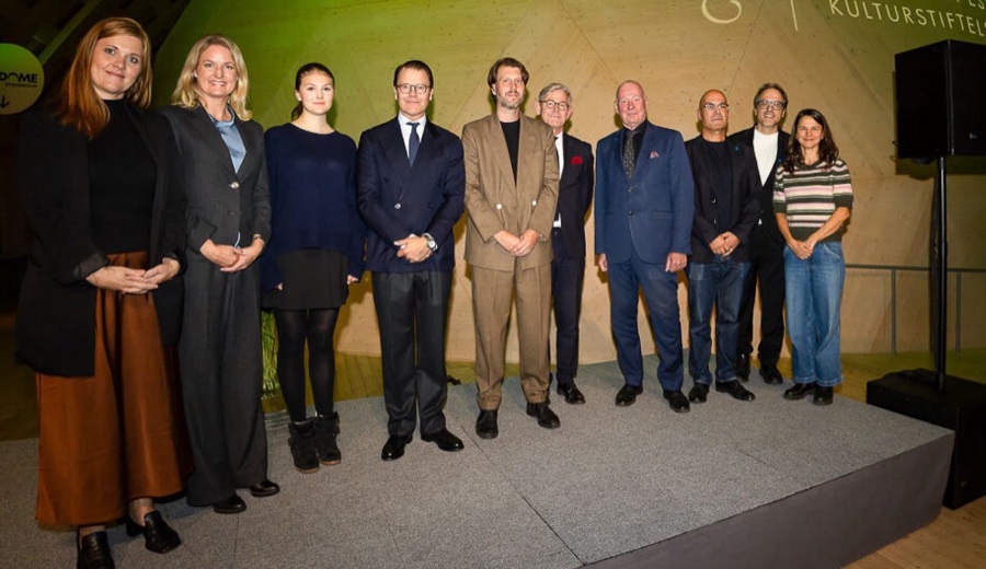 Prince Daniel and Princess Estelle stand with ten others on a stage in front of a wall bearing the Princess Estelle Cultural Foundation logo