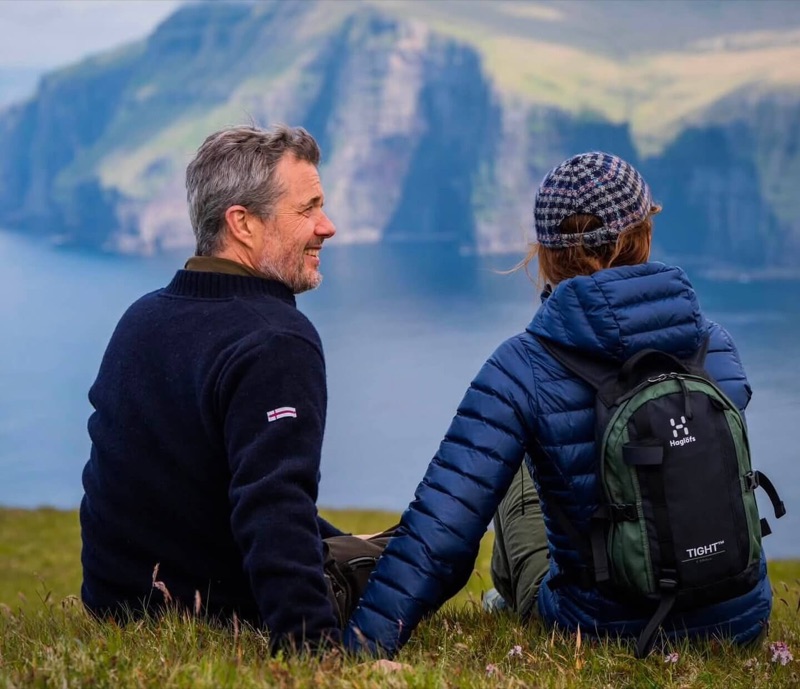 Kongeparet sitter i gresset på en klippe med utsikt over fjordene