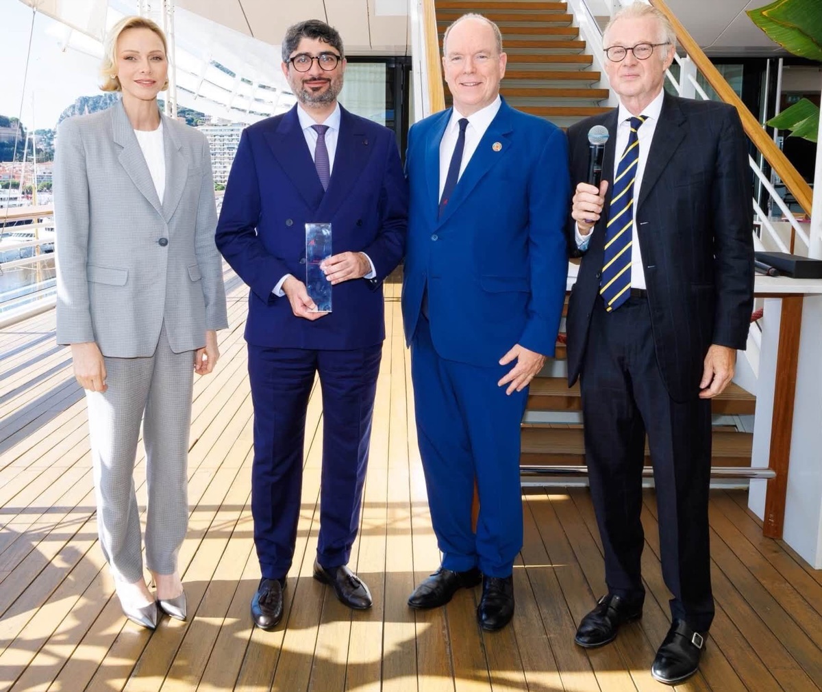 Fyrstinne Charlène, prisvinneren med statuetten, fyrst Albert og en mann med mikrofon stiller opp til bilde