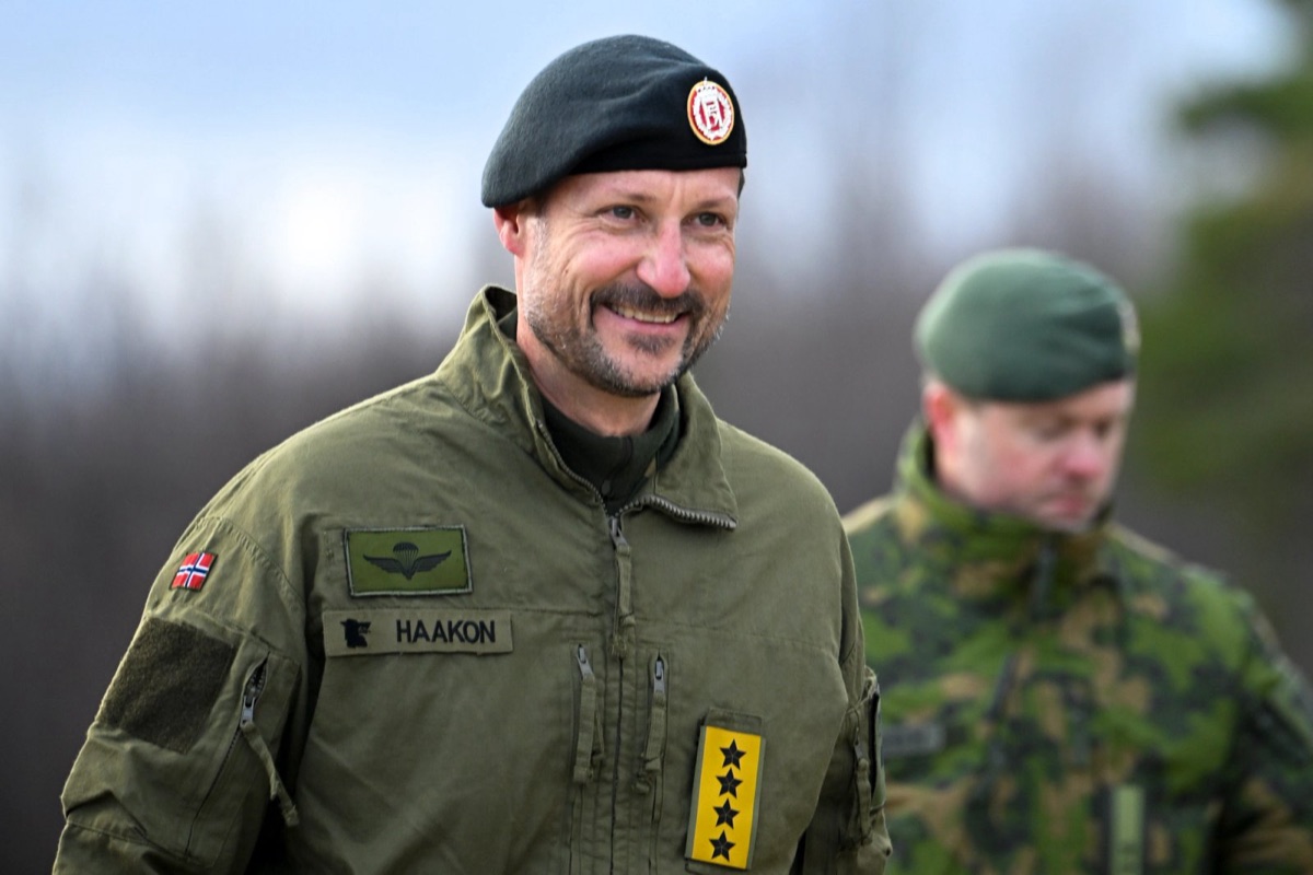 Kong Haakon i uniform smiler, med en offiser i bakgrunnen