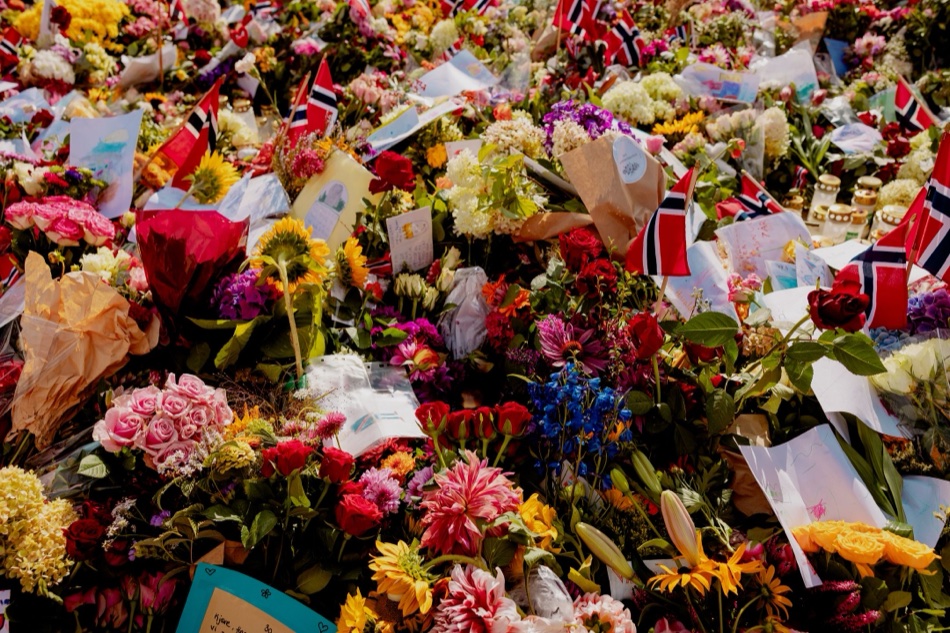 Nærbilde av blomsterhavet med norske flagg, lys, kort og barnetegninger mellom blomstene