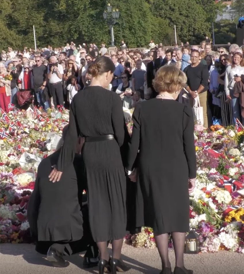 Kongefamilien står ved blomsterhavet på Slottsplassen med ryggen til, mens publikum står tett samlet bak