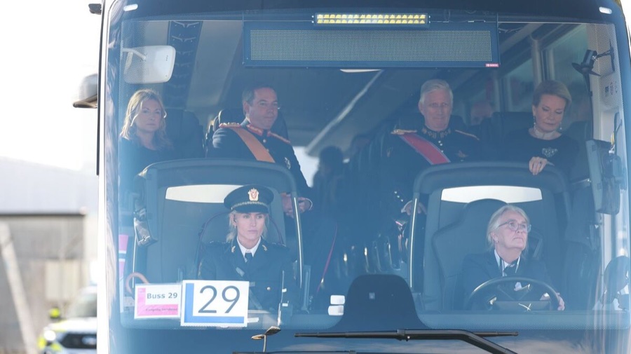 Four people sit in a coach seen through the windscreen, two men in uniform with sashes and two women in black