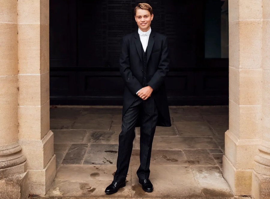 Prince George stands full length between two pale stone pillars in Eton