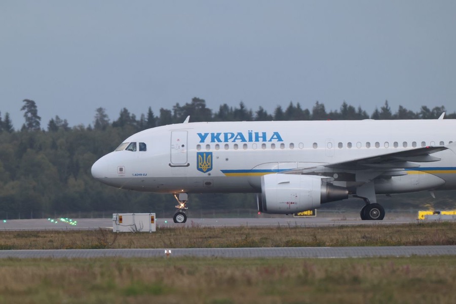 A white aircraft with the word Ukraine in blue and the Ukrainian coat of arms taxis along the runway
