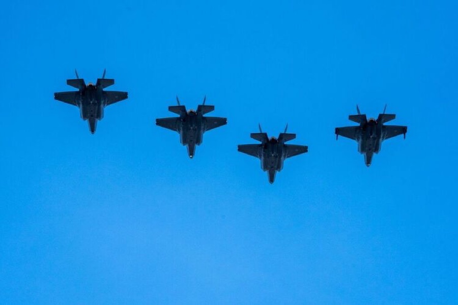 Four F-35 fighter jets fly in formation against a clear blue sky, seen from below