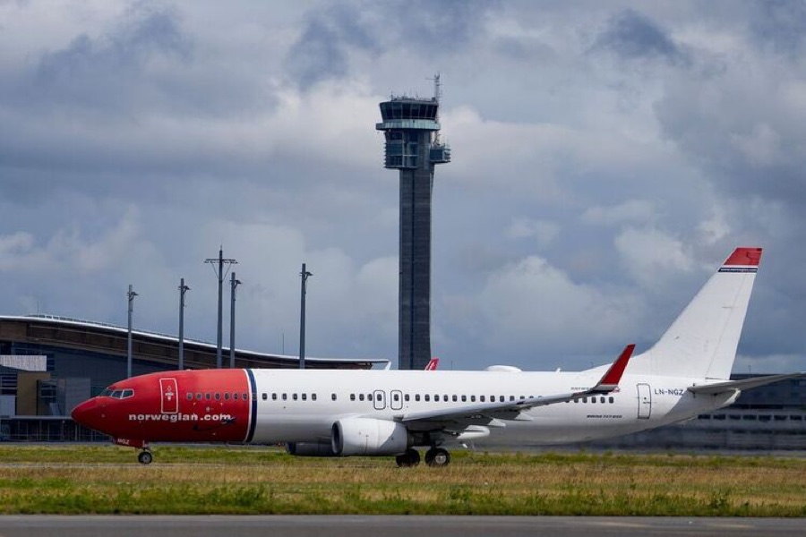 A Norwegian aircraft on the runway at Oslo Airport with the control tower behind it