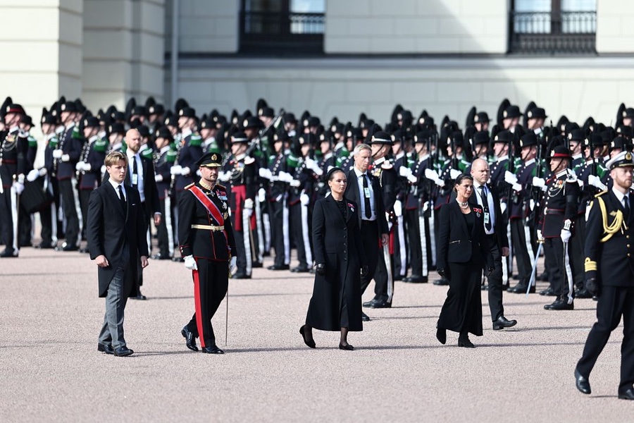 The royal family walk across the Palace Square past ranks of guardsmen, the King in uniform with a red sash