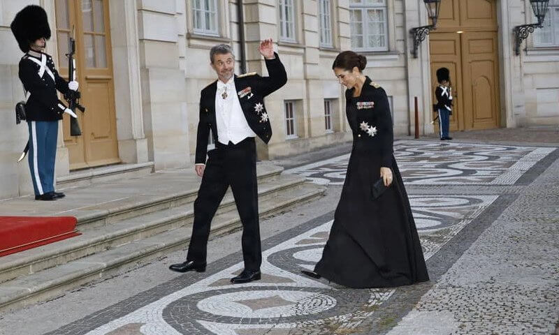 Kong Frederik vinker mens han og dronning Mary går over slottsplassen forbi to gardister