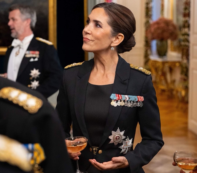 Dronning Mary i uniform med gullepåletter, ordensstjerner og medaljerekke, med et glass i hånden