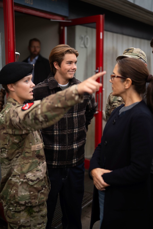 Princess Isabella in uniform points and explains something to Queen Mary, while Crown Prince Christian looks on smiling