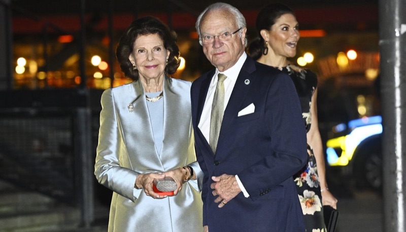 Dronning Silvia i lys silkekåpe og kong Carl XVI Gustaf ankommer konserthuset, med kronprinsesse Victoria bak