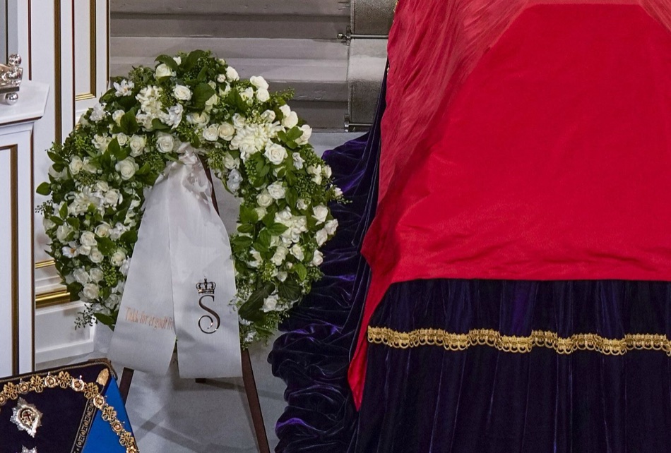 Hvit krans med bånd som bærer dronning Sonjas kronede S-monogram og teksten Takk for et godt liv
