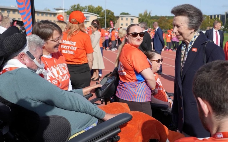 Princess Anne speaks with several participants in wheelchairs beside the track, surrounded by volunteers in orange