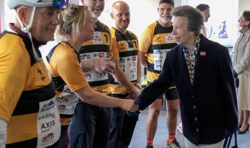 Princess Anne shakes hands with one of the runners, who are wearing yellow and black shirts