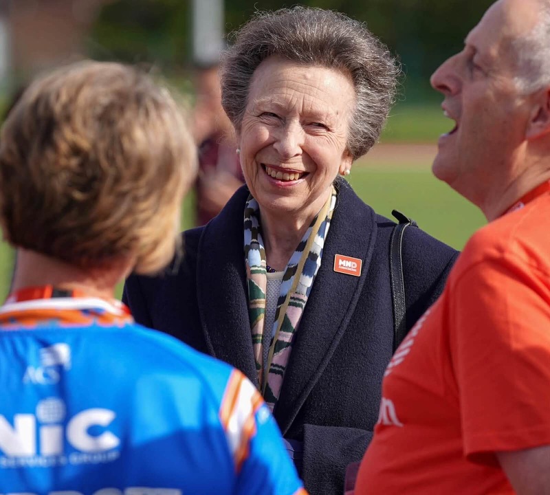 Close view of Princess Anne laughing in conversation, with an MND Association badge on her jacket