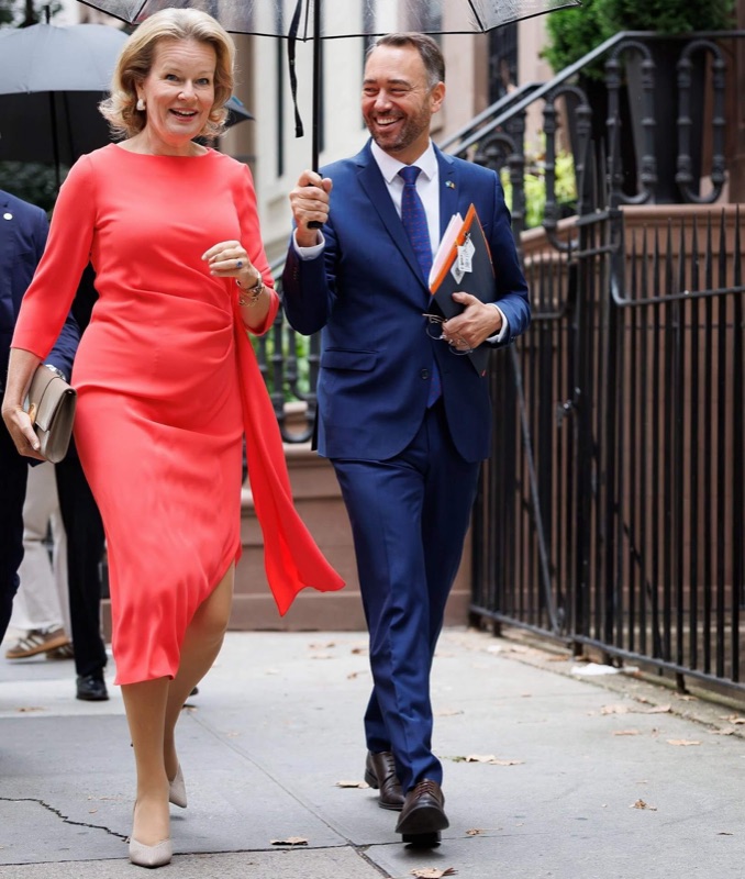 Dronning Mathilde går på et fortau under en paraply sammen med en mann i blå dress