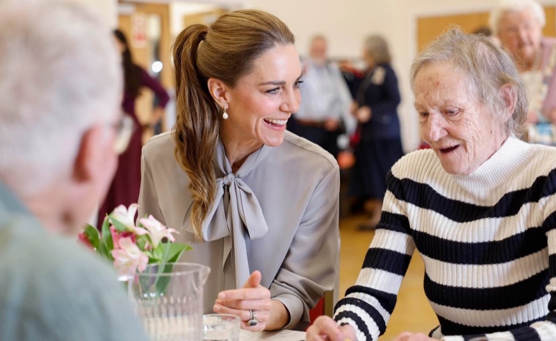 Princess Catherine sits at the table laughing with an elderly woman in a striped jumper