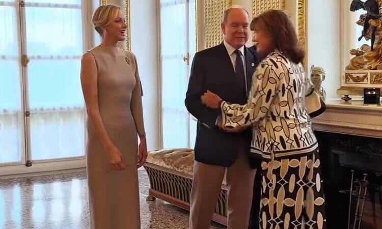 Prince Albert greets a woman in a patterned outfit while Princess Charlène looks on