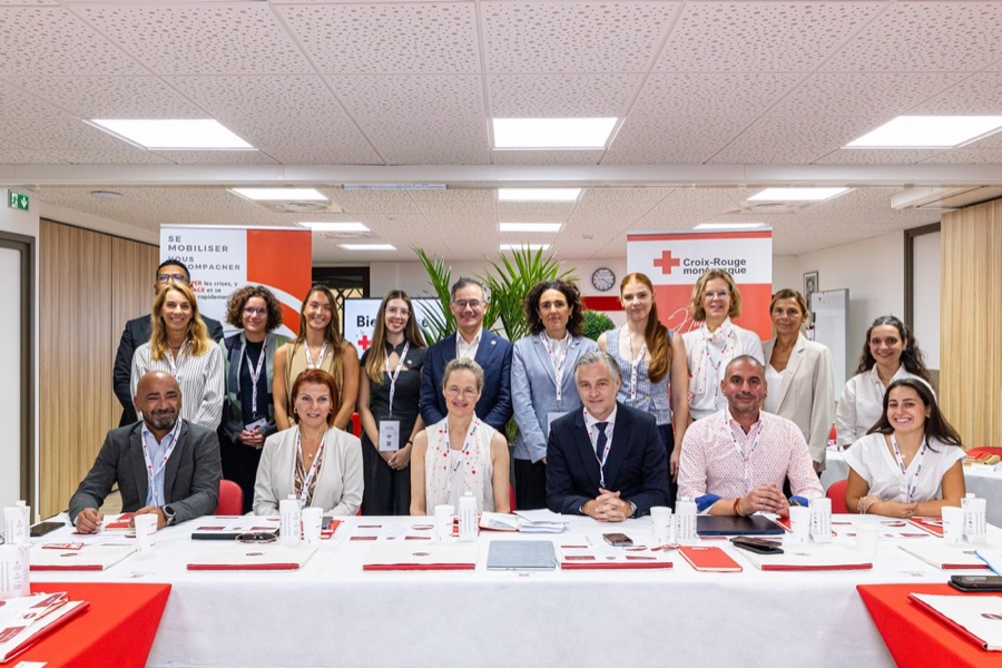 A group of delegates gathered around a long table with red folders in a meeting room at the Monaco Red Cross