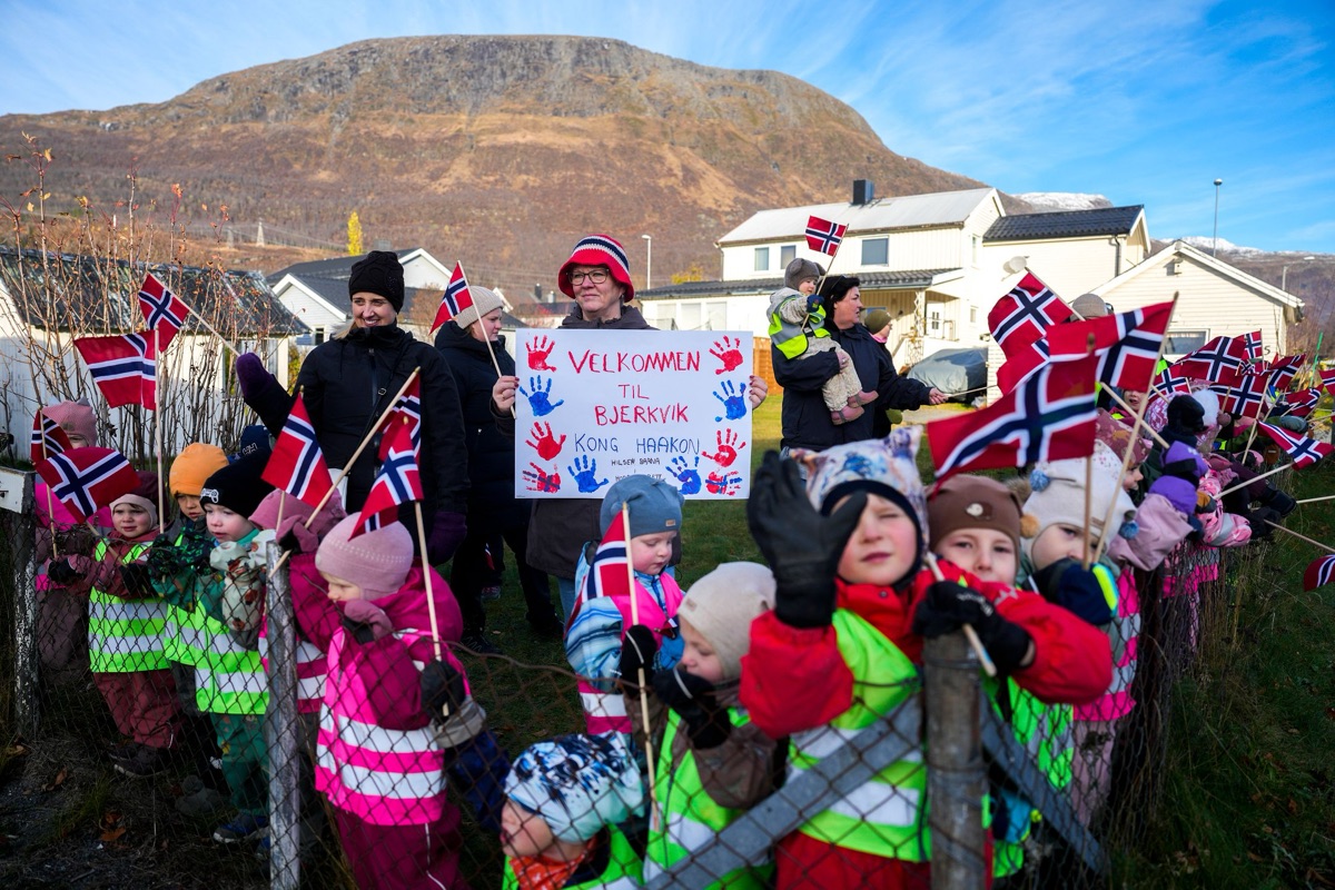 Barnehagebarn med norske flagg og et velkomstskilt venter langs veien