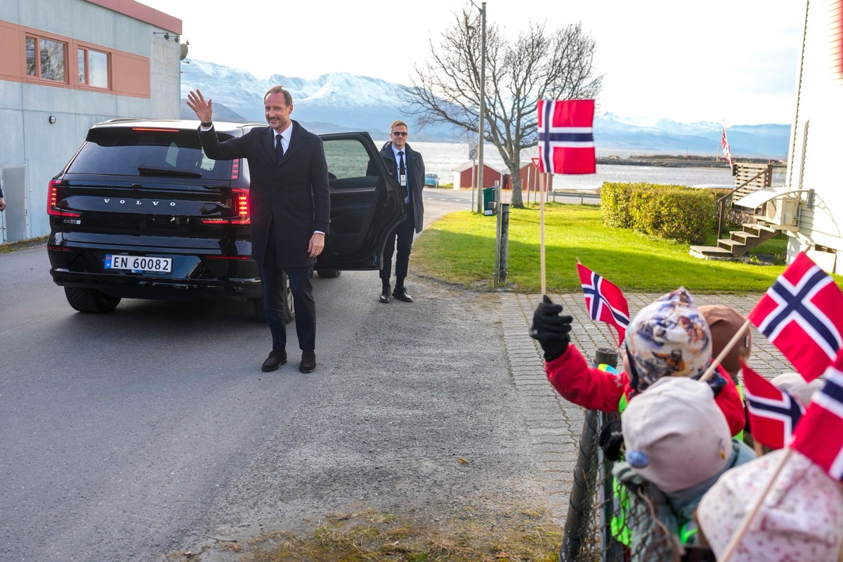 Kong Haakon går ut av bilen og vinker til barn med flagg