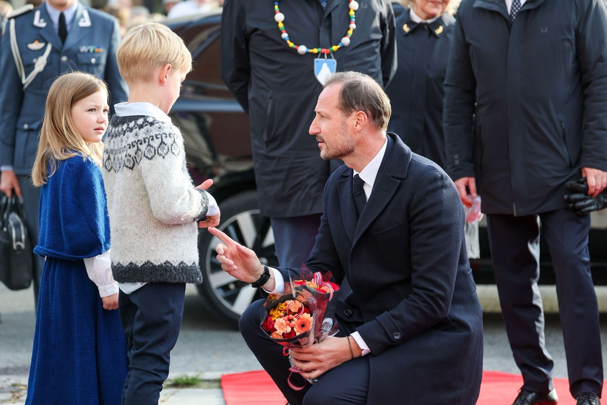 Kong Haakon på huk foran to førsteklassinger som gir ham blomster