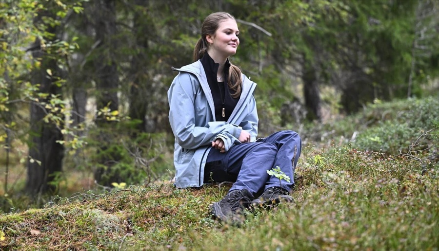 Prinsesse Estelle sitter på en mosekledd skogbunn i lys turjakke og ser til siden