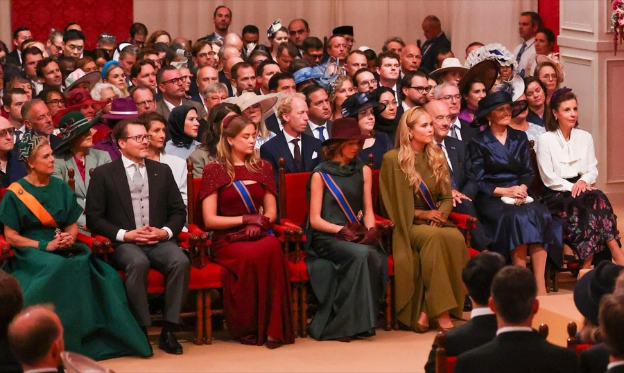 Members of the royal family seated on red chairs in a packed theatre hall